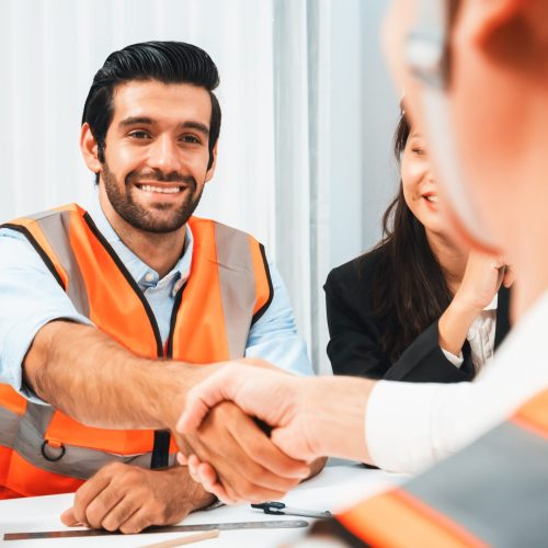 Diverse group of civil engineer and client shakes hand after make successful agreement on architectural project, reviewing construction plan and building blueprint at meeting table. Prudent